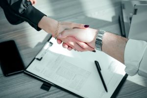 Two people shaking hands over a signed contract